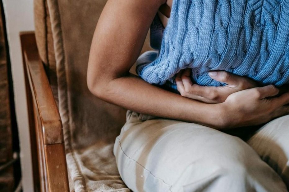 Una mujer retorciéndose de dolor mientras está sentada.